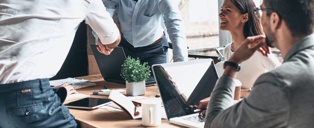 Two men shaking hands at business meeting with cmales & female colleagues seated : Health & Safety Consultancy from JCM Health & Safety, Liverpool.