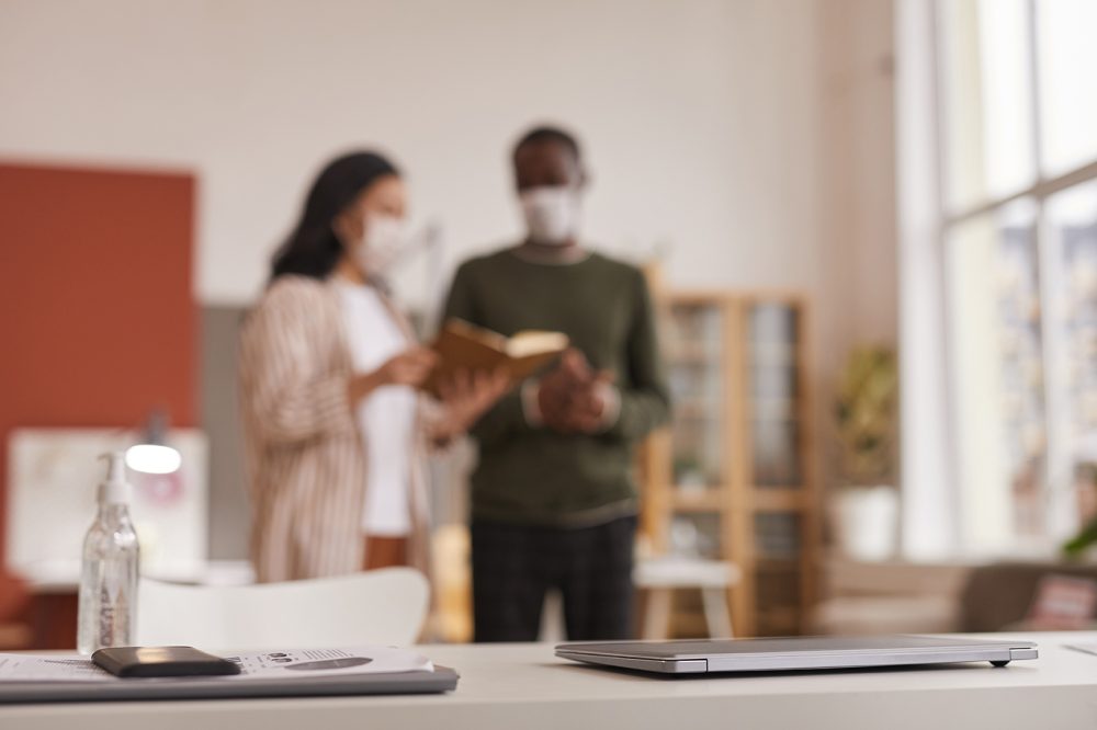 Blurred man & woman, both wearing masks, looking at a book in a meeting room : Health & Safety Consultancy from JCM Health & Safety, Liverpool.
